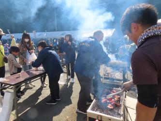 網の上で食材を焼く男性や参加者に食べ物を手渡す女性の写真