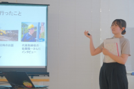 スクリーン画面に映し出された資料を身振り手振りで説明をしている女性の写真