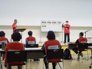 1級指導者の方がホワイトボードに書かれた資料を元に説明をしていて、座って聞いている関係者達の写真