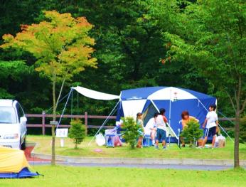 緑の木々に囲まれた芝生の上にテントを設置し家族で賑わっている写真