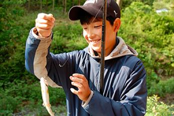 帽子をかぶった男の子が釣れた魚を嬉しそうに見ている様子の写真