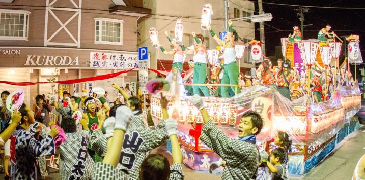 船山車に乗り晒しを巻き緑のズボンを着た方達が元気良く踊っており、下の道路で法被を着た方達が踊っている祭りの様子の写真