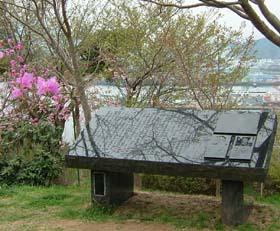 手前にピンクの花が咲き、臼木山に「宮古湾海戦解説碑」が設置された写真