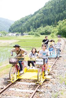 参加者達が2号と書かれた黄色のレールバイクを先頭に線路の上を走っている写真