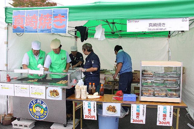 真崎焼きとと書かれたテントの中で5名の人たちが商品を焼いたり詰めたりしている写真
