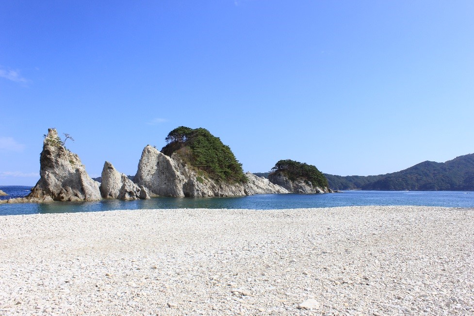 白い砂浜の奥の波打ち際に大きな岩がある風景写真