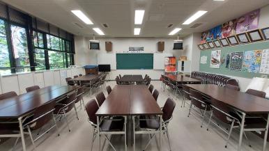 前方に黒板が設置された、縦に三列の6つの長机と椅子が置かれた集会室の写真