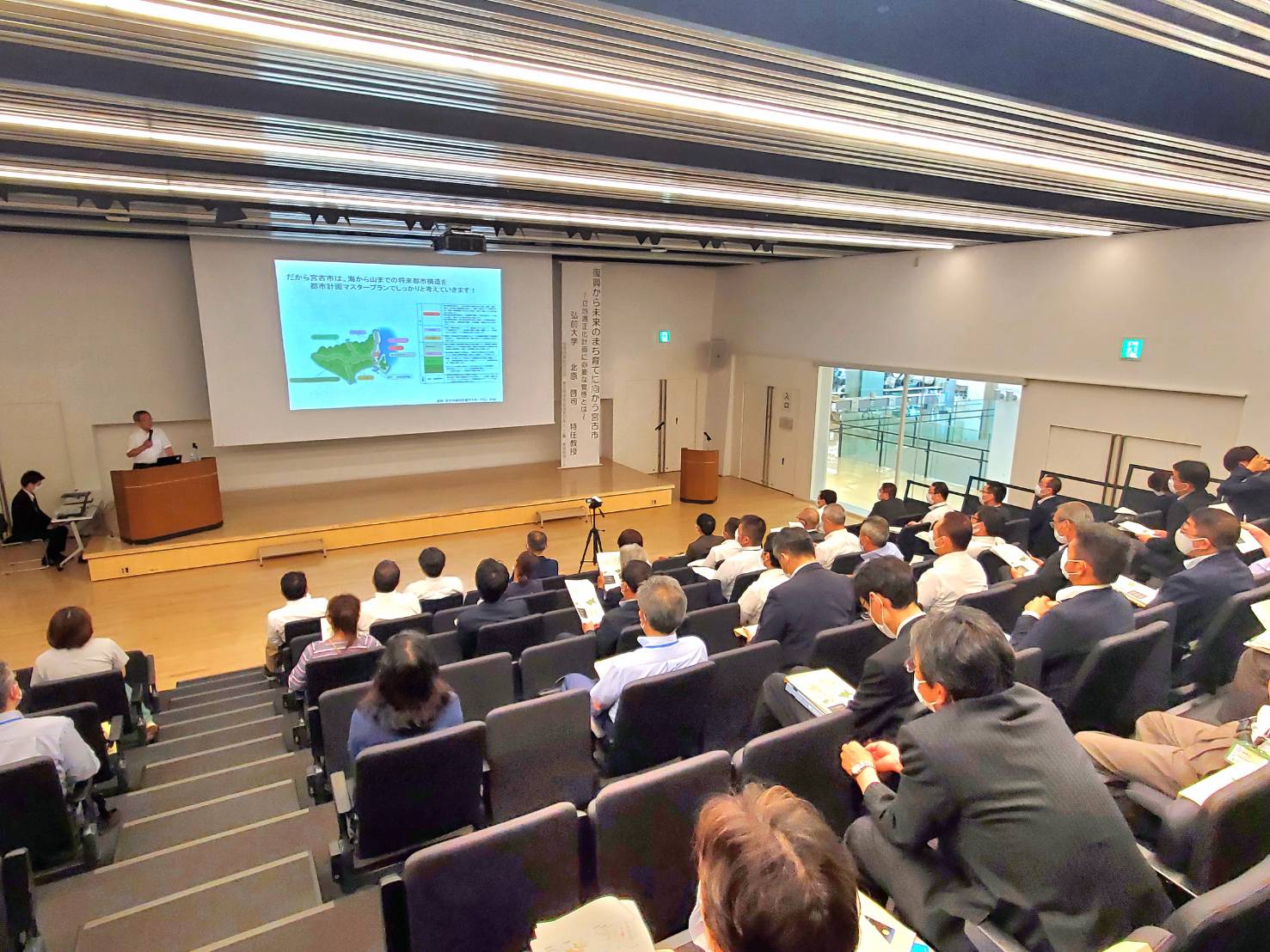北原先生が舞台でスクリーンを使いながら講演を行っている様子を写した写真