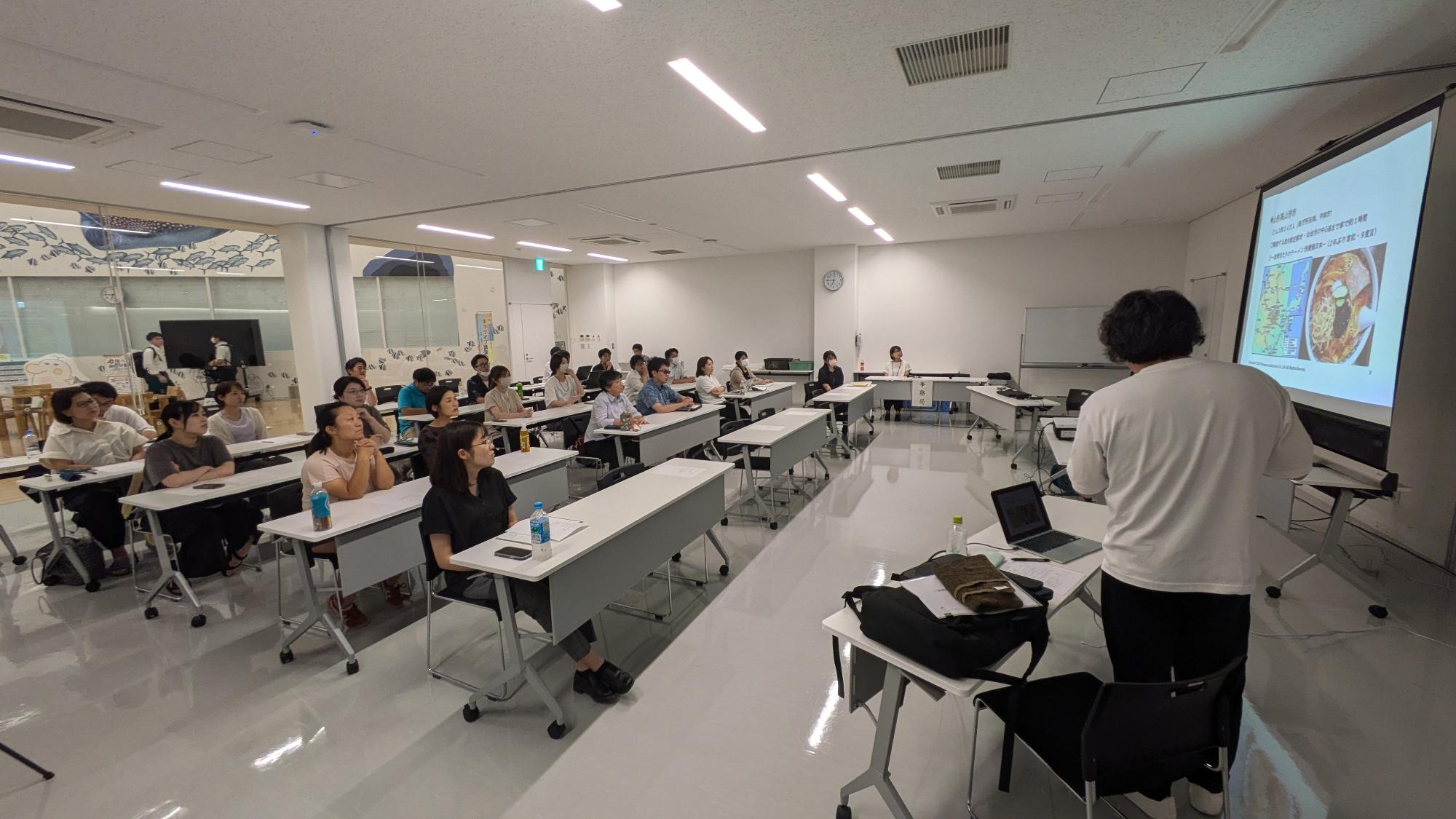 キックオフ会議でセミナー形式で講師の話をきく参加者