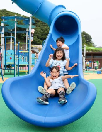 青い滑り台から3人の子供たちが着地しようと笑顔で楽しんでいる写真