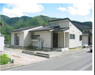 山に囲まれ、クリーム色の外壁の川井団地住宅の外観写真