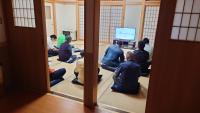 畳に直に座り、前方の小さなモニターを見ている説明会の参加者の人たちの後方から写した写真