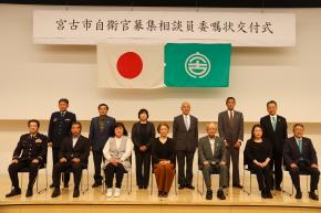 宮古市自衛官募集相談員委託状交付書かれた幕の下に1列目は椅子に座っている7名の方、2列目は6名の方が立っている舞台を写した写真