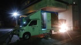 暗闇の中トイレカーの周りに照明が灯されている写真
