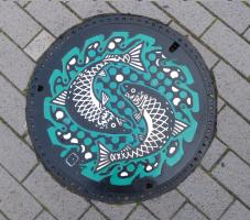 二匹のサケが円を描くように書かれているマンホールが宮古第一中学校前交差点歩道に設置されているのを上から写した写真