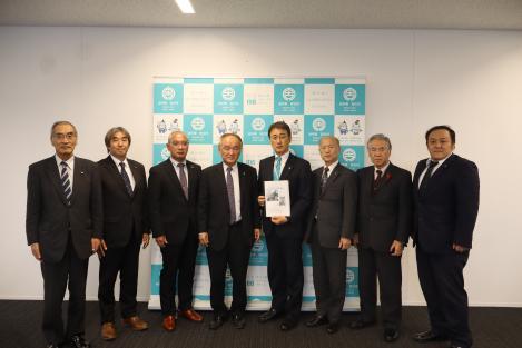 橋本議長、竹花副議長、総務常任委員他関係書の方々8名が横一列に並び、中央に立つ桐田副市長が提言書を持って写っている写真