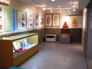 壁に数多く資料が展示され、その下に展示物が置かれたショーケースと銅像が設置されている展示室内の写真