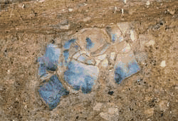 土の中に黒色でヒビが入り破損がみられる土器が表面だけ見え埋まっている写真