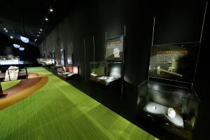 薄暗い室内にいくつも設置されたショーケースの中に貝塚から出土した展示物がスポットライトに当たっており、そのケースの上に説明資料が壁に設置されている展示室内の写真