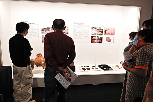 壁やテーブルの上に展示された資料や展示物を参加者が眺めている写真