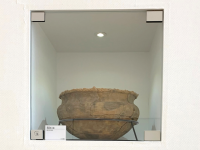 白い箱型の中央に展示された肌色に灰色がかった模様で丸みがある植木鉢のような形の縄文土器を撮影した写真