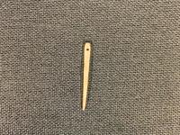 灰色の背景の中央に置かれた鹿の骨で作られた通常の針より少し幅があり平たく見えるが形が整えられている縫い針をアップで撮影した写真