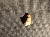灰色の背景に照明の強い光が当たり、上部に小さい丸い穴が開いている日本オオカミの臼歯から作られたペンダントをアップで撮影した写真