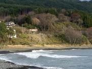 切り開かれた山の中腹に民家が建ち、目の前に海が広がっている写真