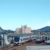 側面に白地に赤ラインで模様が描かれた観光列車「ひなび(陽旅)」が停車している様子を正面から撮影した写真