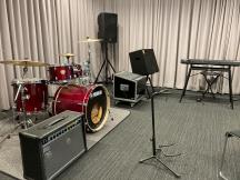 奥にキーボードがあり、左側に赤色のドラムセットが設置された音楽スタジオ内の写真