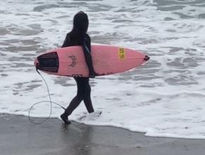ウェットスーツを着用し、サーフボードを片手に持った選手が海に入ろうとしている写真