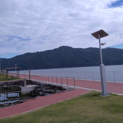 後方に山々が見える海沿いの遊歩道の写真