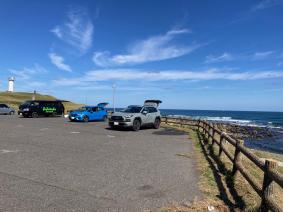 広大な海が広がる海岸に沿った駐車場で海が見えるようにバックドアをあけて停車している3台の車の写真