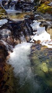 小さな滝に水が流れ、ところどころ雪が積もっている水辺の写真