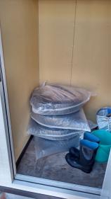 バケツやレインブーツと一緒に、1本ずつ大きなビニール袋に入った4本のタイヤが積まれている倉庫内の写真
