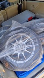工具箱や大きなビニール袋に入ったタイヤが、ビニールシートが敷かれた車の後部座席に置かれている写真