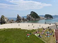 快晴の空の下、浄土ヶ浜の絶景と砂浜で遊ぶ人たちや、芝生広場でヨガを楽しんでいる人達を高台から撮影した写真