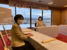 海が見える大きな窓が設置された宮古商工会議所創業スクールの会場で、テーブルクロスが掛けられた長机の席の奥と手前に2名の女性が座っている写真
