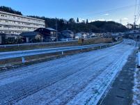 川を挟んだ左側に団地や住宅街が建ち、夜中に降った雪が凍った細い道路を撮影した写真
