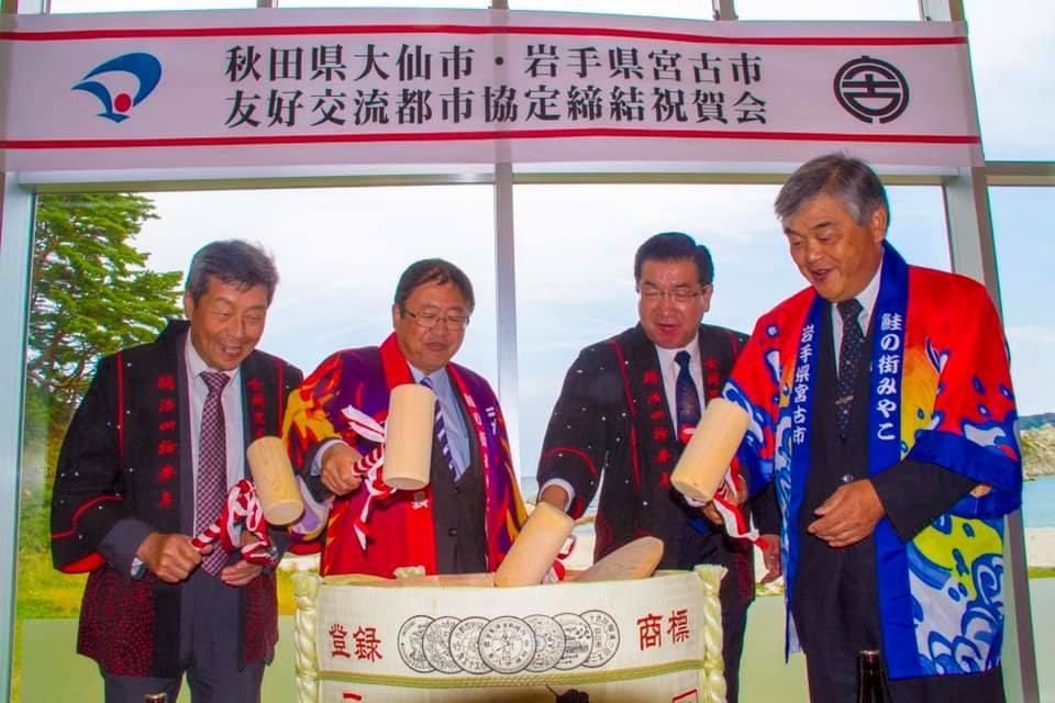 秋田県大仙市・岩手県宮古市友好交流都市協定締結祝賀会の横断幕の下で、鏡開きを行う金谷大仙市議長、山本宮古市長、老松大仙市長、古舘宮古市議長の写真