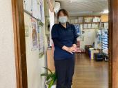左の壁にポスターが貼ってある建物の入り口に、黒に紺色の服を着た女性が立っている写真
