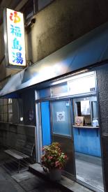 「福島湯」と書かれた点灯した看板が壁に設置され、引き戸が開けっ放しになっている銭湯の入り口の写真
