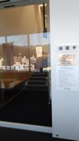 反射した市街地が写っている透明なガラスの右側に「会議中」と書かれた議会会場の写真
