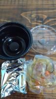 「前沢牛入り釜めし」の商品に入っていた黒色の丼容器と透明の蓋、具材が入った銀色の袋と透明袋を並べた写真