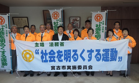 「社会を明るくする運動」と書かれた横断幕を持つ市長とオレンジ色のジャケットを着た関係者の方々の写真