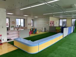 室内用の芝のような床材が敷かれた場所と、その奥に見える小さめの遊具が置かれた場所の写真