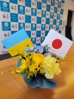 黄色と水色のアレンジメントフラワーにウクライナと日本の国旗が飾られている写真