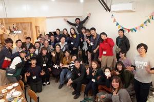 広い部屋の中で、楽しそうにピースサインをしたり笑ったりしている30人ほどの男女の集合写真