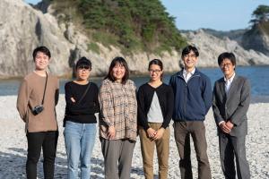 海辺で横一列に並んで笑っている6人の男女を正面から写した写真