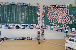 左の黒板に書かれた文字と、右の黒板には花びらのメモ帳のようなものが沢山貼ってあり、その2つの黒板の外枠に沢山の写真が貼り付けられている写真